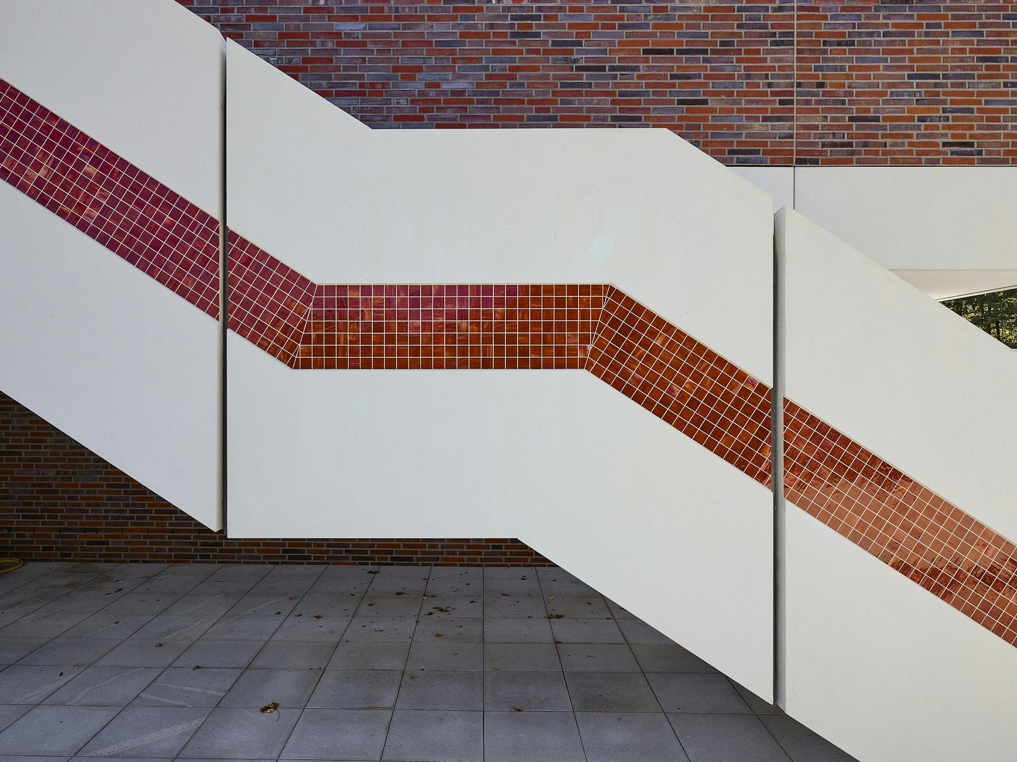 Photo: Detail of an external staircase which leads to the second floor of DAS MINSK. The staircase is covered with white panels in which red mosaic pieces are embedded.